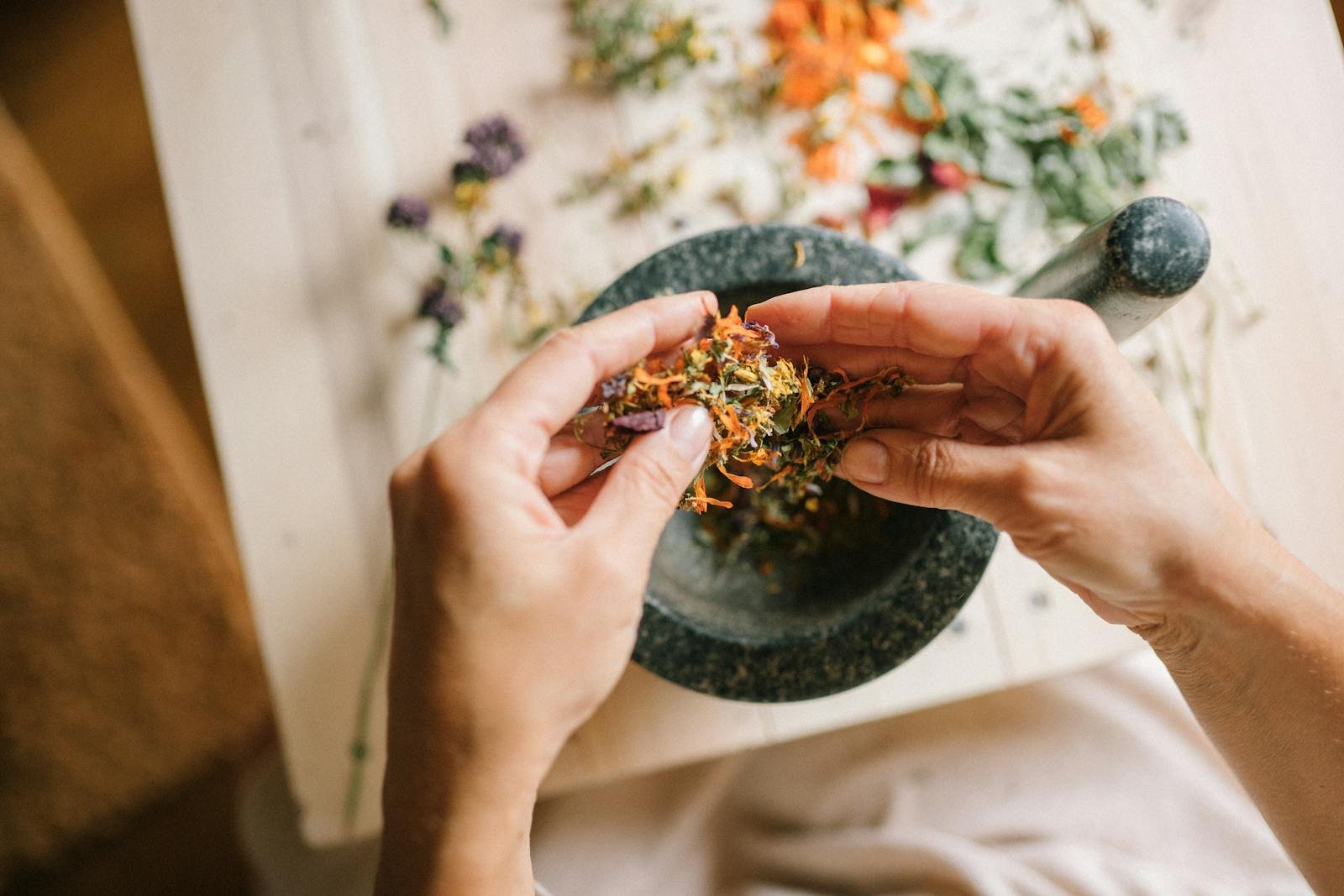 Close-up of hands preparing herbal ingredients in a mortar and pestle, top view.